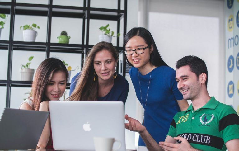 Team Dorka24 Vier Personen betrachten gemeinsam einen Laptop in einem modernen Büro.